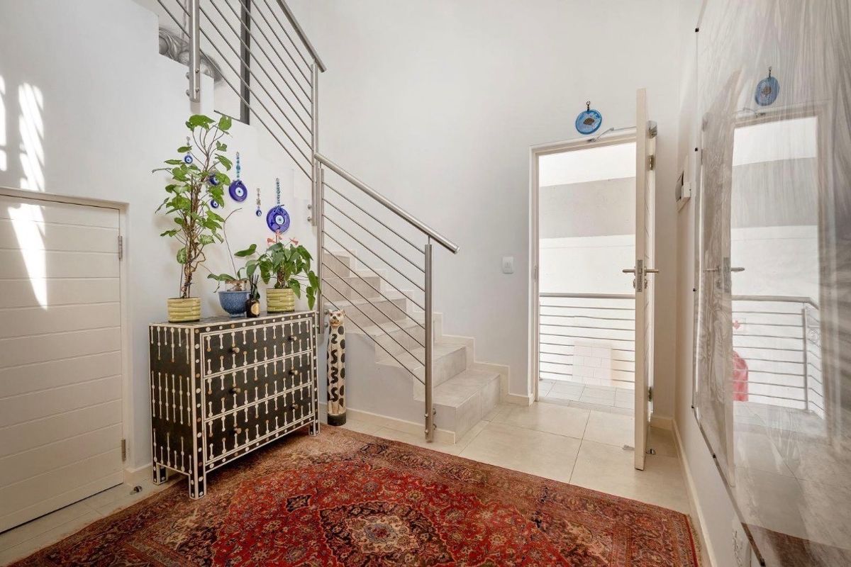 Bright entrance foyer featuring a modern staircase with stainless steel railings and neutral tiled flooring, leading directly to an external door.
