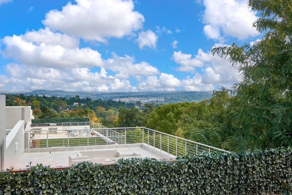 Elevated view from a terrace overlooking lush green hills and a distant cityscape under a bright blue sky.