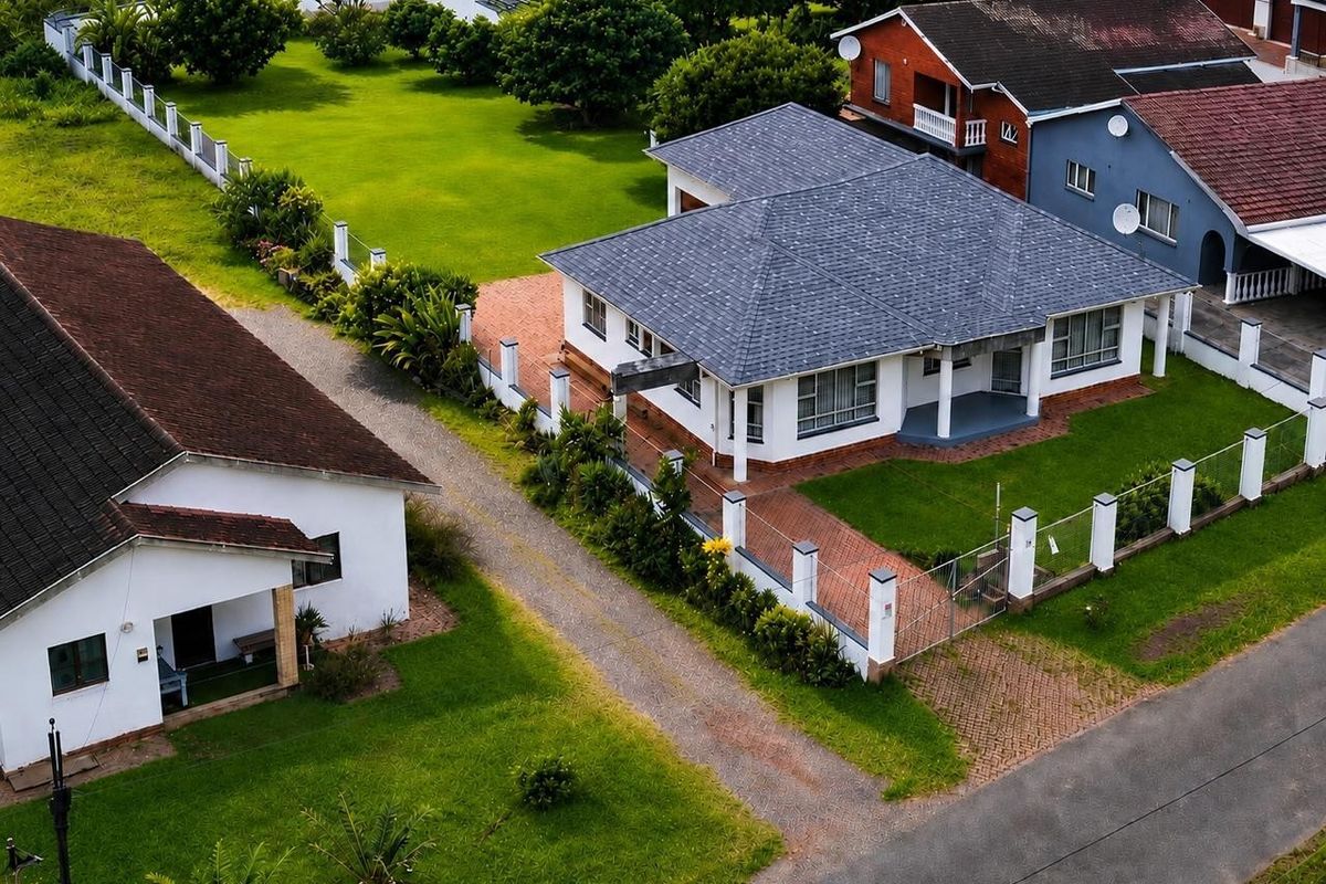 Aerial view of a well-maintained residential property featuring a spacious lawn, paved driveway, and a house with a modern asphalt shingle roof.