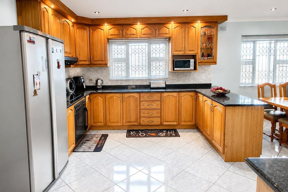A well-maintained kitchen featuring warm wooden cabinetry, granite countertops, built-in appliances, and tiled flooring, offering a functional and classic cooking space.