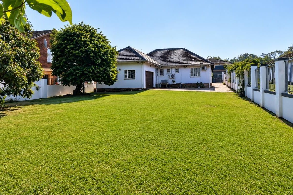 A spacious rear garden featuring a well-maintained lawn, perimeter boundary walls, and a paved driveway leading to the garage.