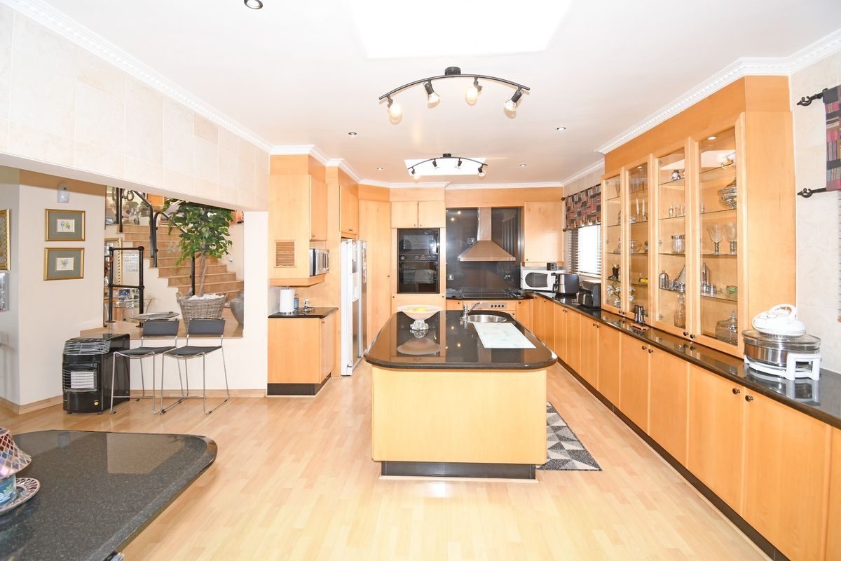 Spacious kitchen featuring light wood cabinetry, a central island with granite countertops, built-in appliances, and ample storage with glass-front display cabinets.