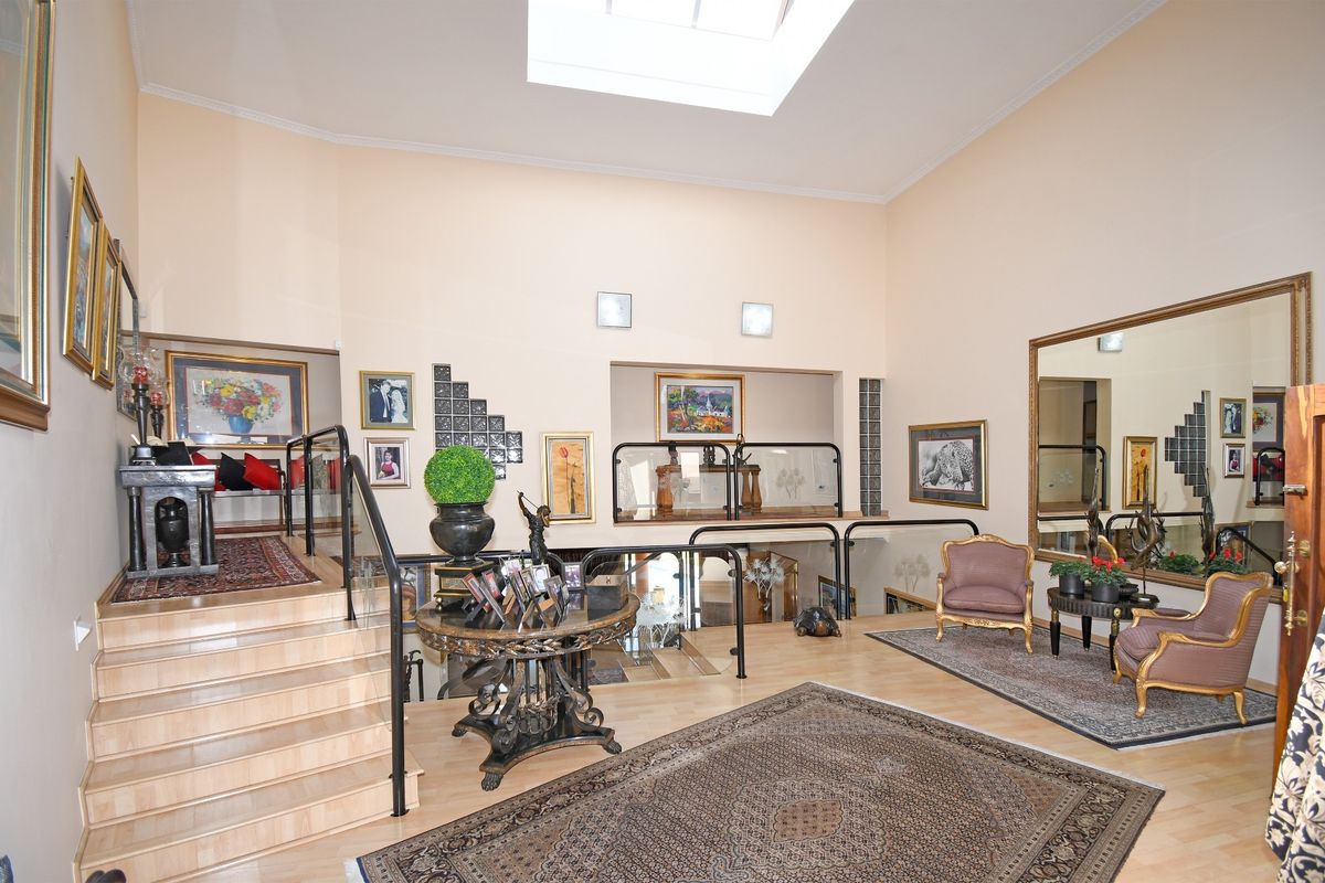 Spacious living area featuring high ceilings with a skylight, laminate flooring, and a split-level layout with modern glass balustrades.