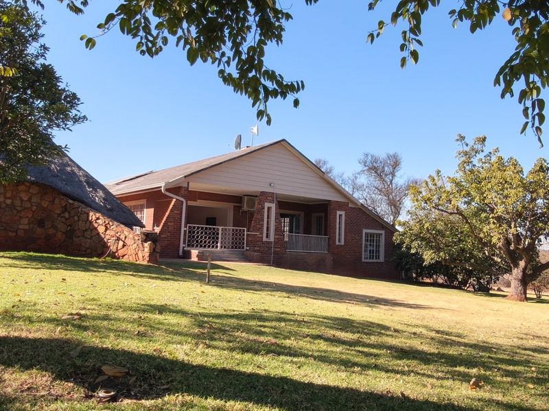 Rear view of a brick-faced small holding property featuring a covered patio, a combination of tiled and thatched roofing, and expansive garden grounds.