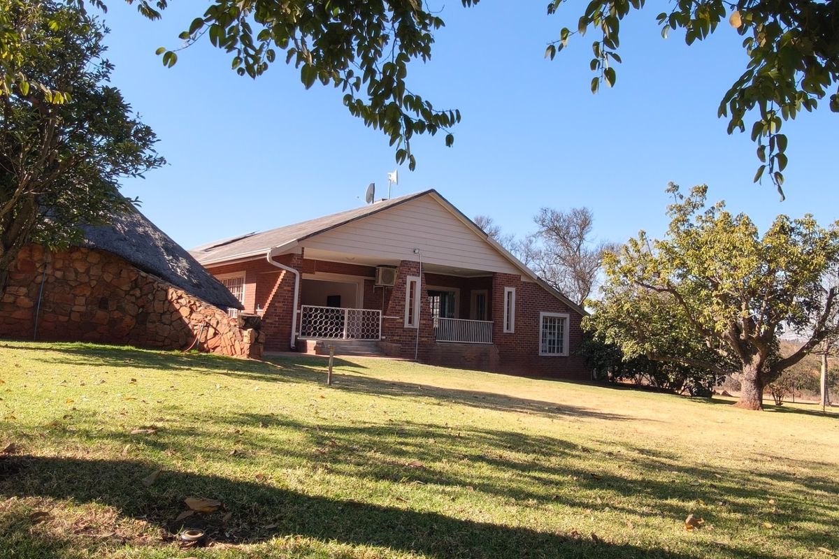 Rear view of a brick-faced small holding property featuring a covered patio, a combination of tiled and thatched roofing, and expansive garden grounds.