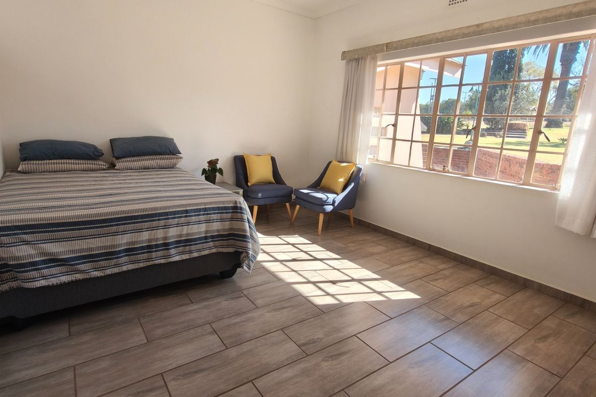 A bright and spacious bedroom featuring modern wood-look tiled flooring and a large window that allows for ample natural light.