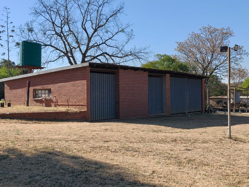 A detached face brick garage building featuring multiple roller doors and an elevated water storage tank, situated on a large open plot.