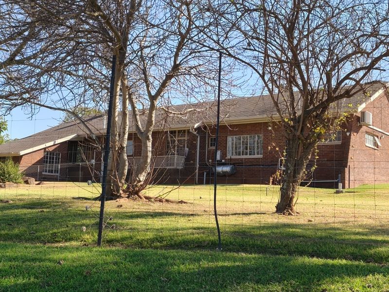 Rear view of a brick-built small holding residence featuring a tiled roof, external geyser, and air conditioning unit, set within a fenced garden area.