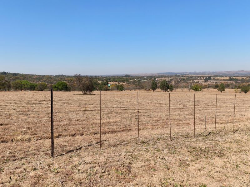 Expansive view of the open small holding landscape featuring dry grazing land and perimeter wire fencing under a clear blue sky.