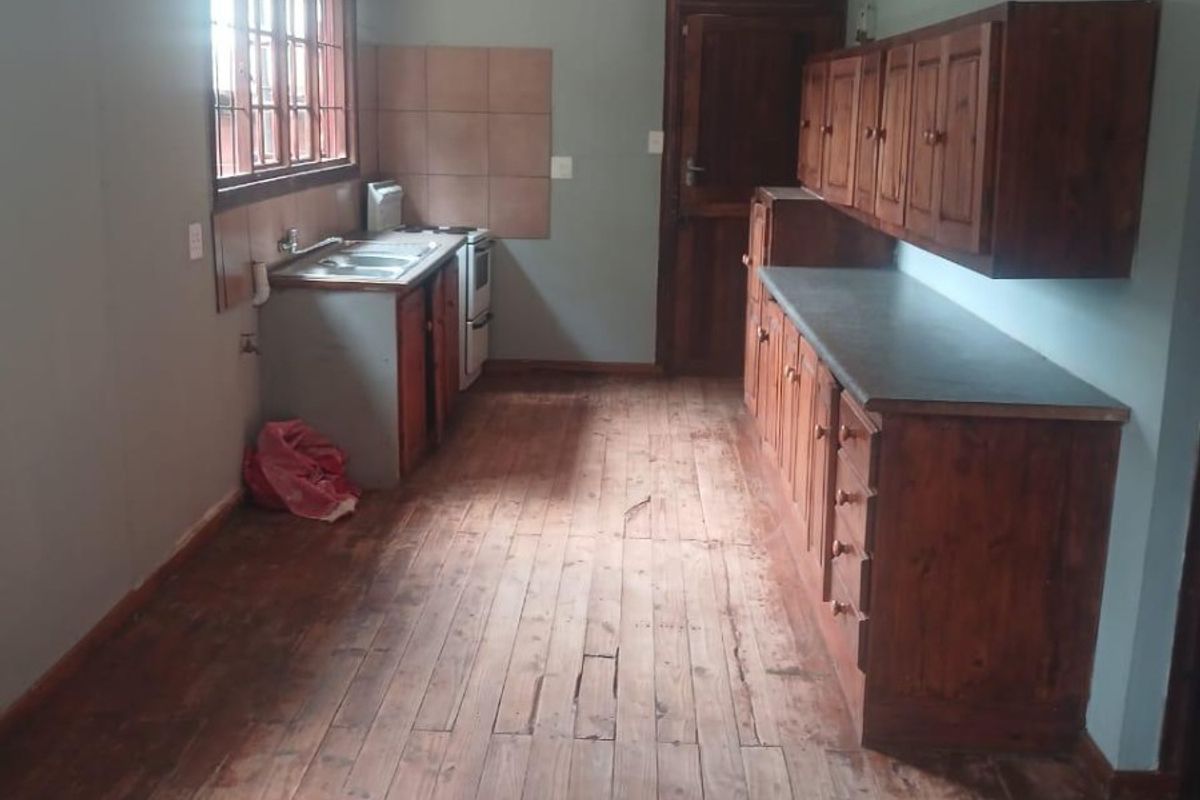 A functional kitchen featuring timber cabinetry, laminate countertops, a stainless steel sink, and original timber flooring, offering potential for modernization.