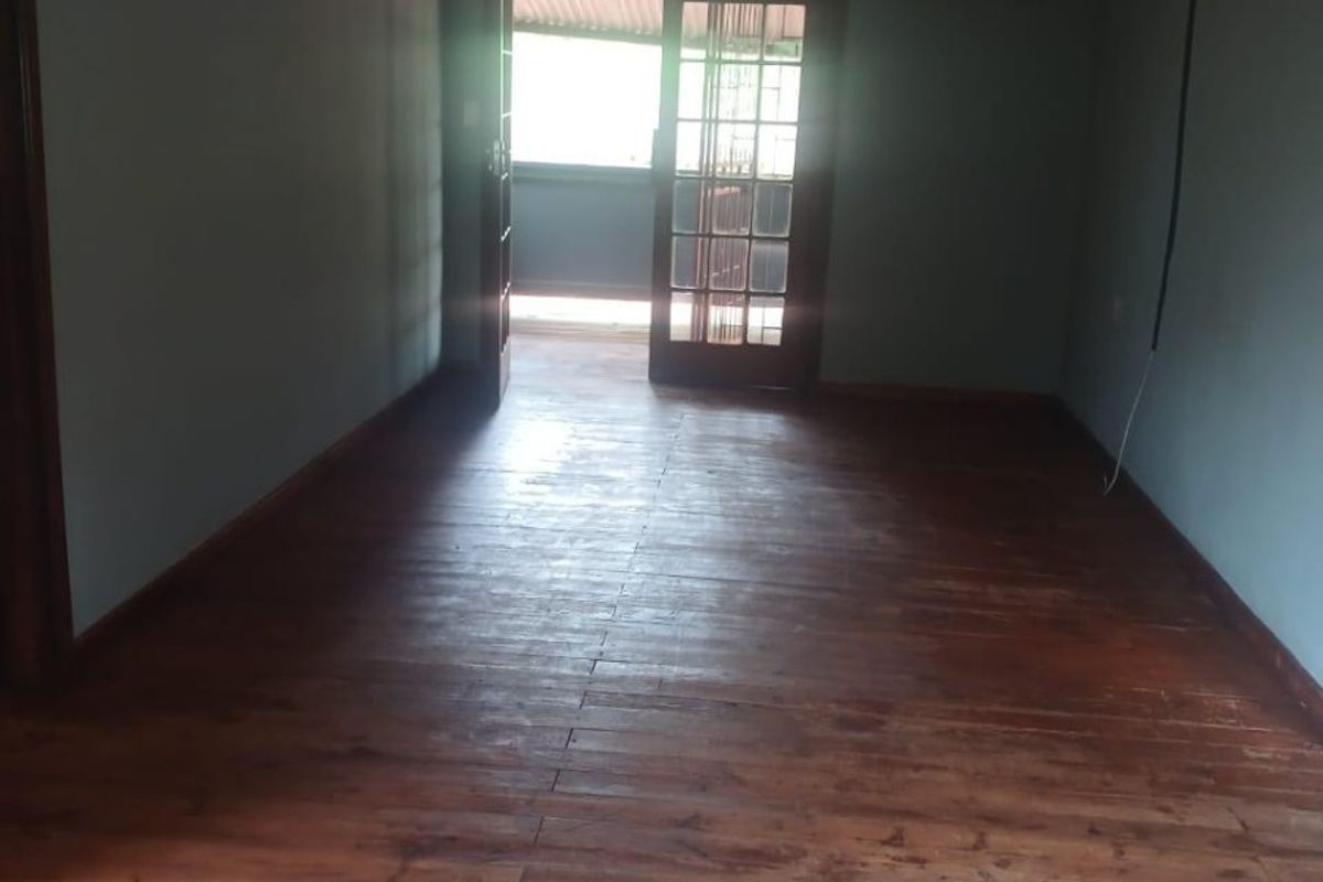 An empty living room featuring wooden flooring, an air conditioning unit, and french doors leading to an outdoor area.