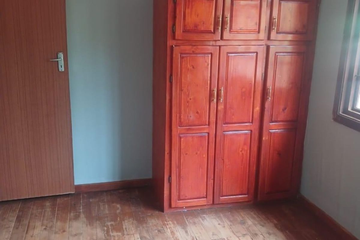 A bedroom featuring original wooden flooring and a built-in wooden wardrobe, requiring cosmetic updates to the flooring and wall finishes.