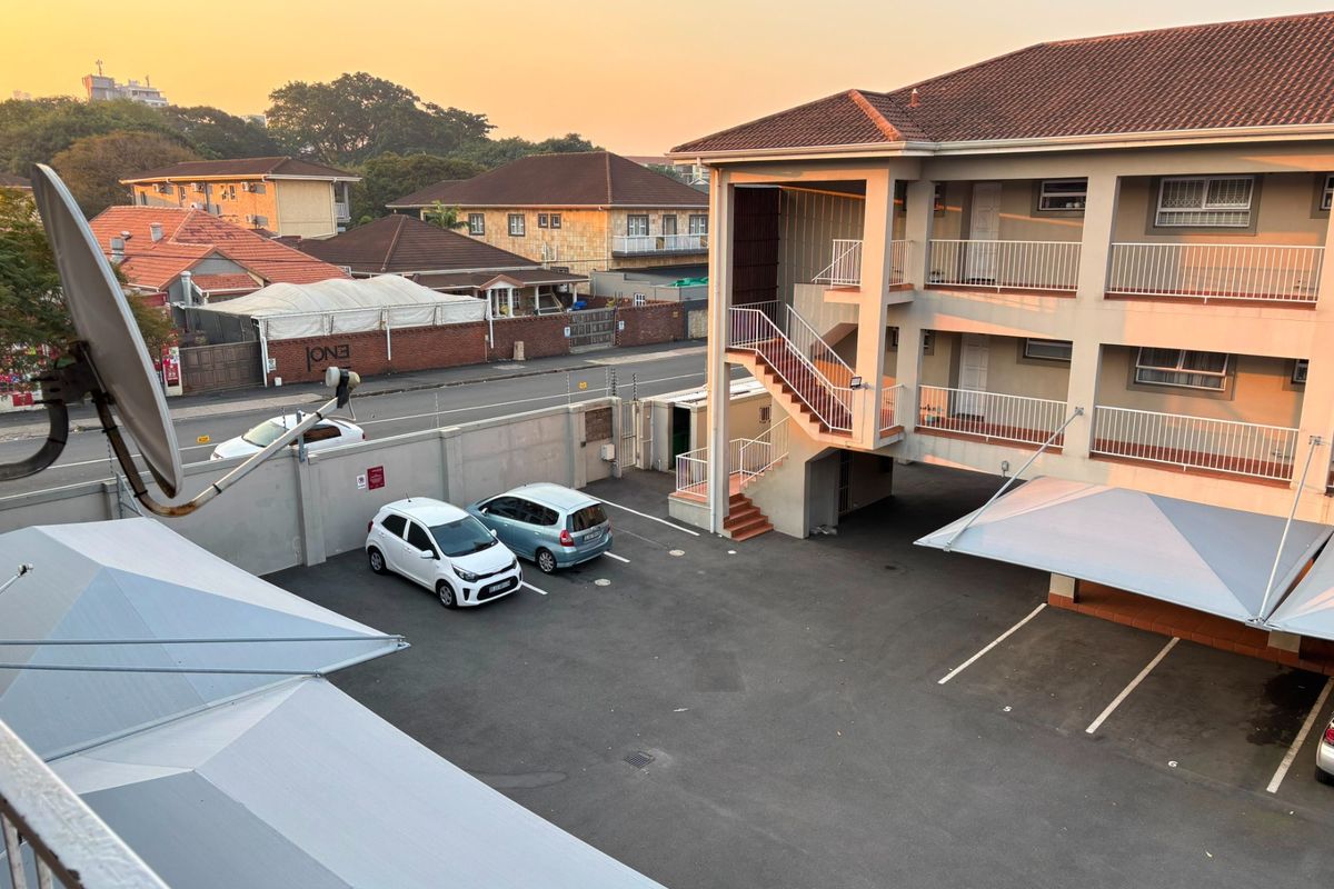An elevated view of the apartment complex parking area, featuring covered carports, external staircases, and secure perimeter walling.
