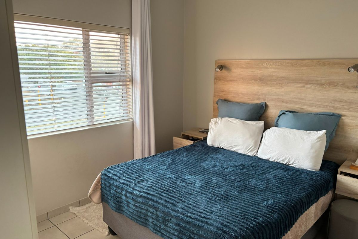 A well-maintained bedroom featuring tiled flooring, a built-in wooden headboard, and venetian blinds, offering a clean and functional living space.
