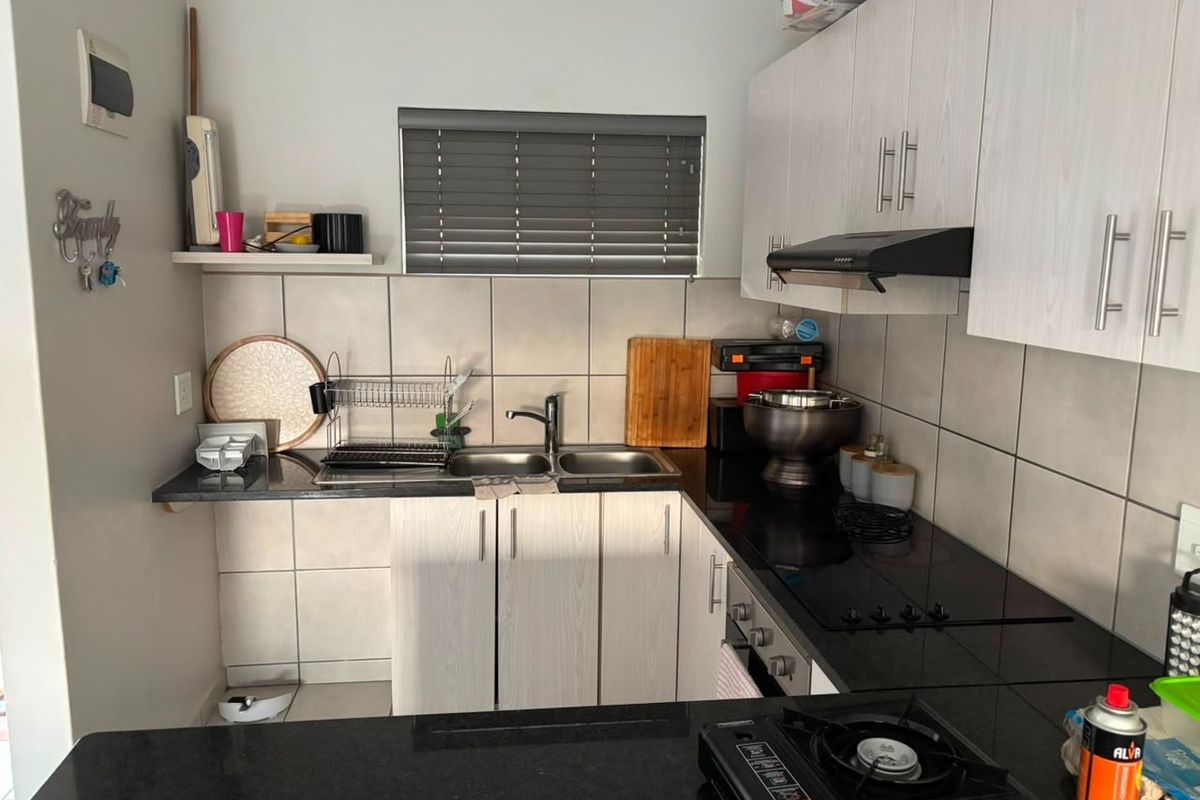 Compact kitchen featuring black granite countertops, built-in oven, electric hob, extractor fan, and light-toned veneer cabinetry with a tiled backsplash.