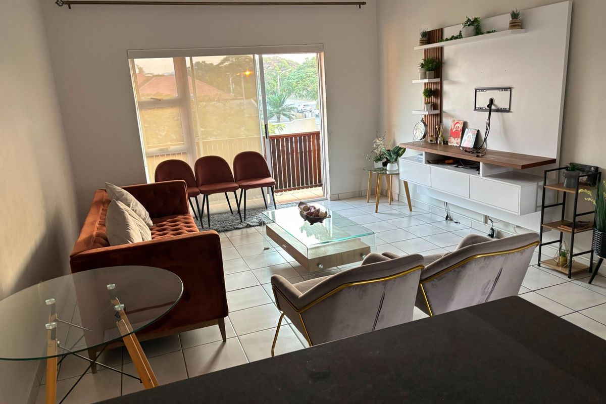 A bright living room featuring tiled flooring, a built-in media console with floating shelves, and a sliding glass door leading to a balcony.