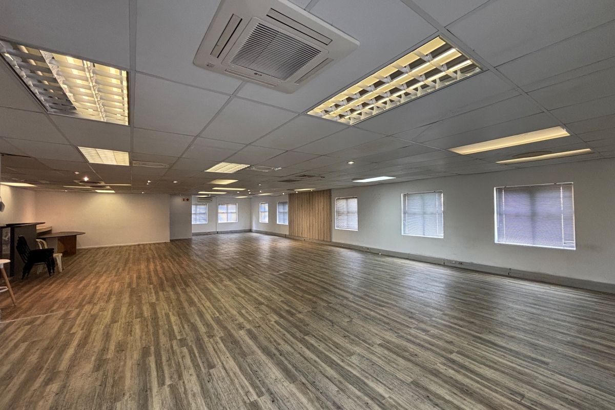 A spacious, open-plan office area featuring wood-look vinyl flooring, suspended ceilings with recessed lighting, and integrated cassette air conditioning.