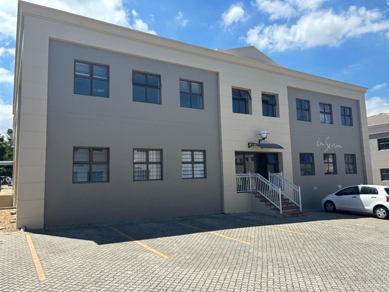 A well-maintained multi-story office building exterior featuring a paved parking area, modern facade, and a clearly defined entrance with staircase access.