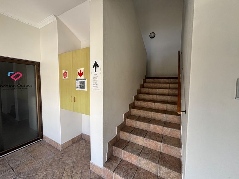 A functional office building hallway featuring a tiled staircase with a wooden handrail and a built-in storage cupboard.