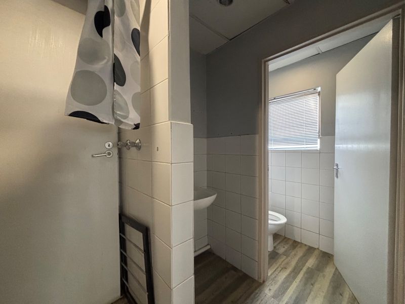 A functional bathroom space featuring a wall-mounted basin, toilet, tiled splashbacks, and wood-look flooring, currently requiring minor cosmetic finishing and updates.