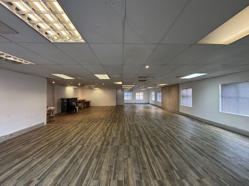 A spacious, open-plan office area featuring wood-look vinyl flooring, recessed lighting, and a wood panel feature wall, offering a versatile workspace.