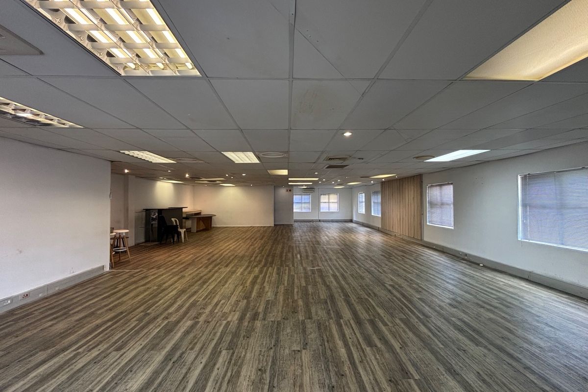 A spacious, open-plan office area featuring wood-look vinyl flooring, recessed lighting, and a wood panel feature wall, offering a versatile workspace.