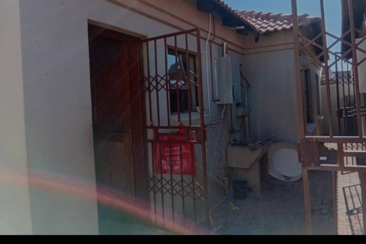 Rear exterior view of the apartment featuring a paved courtyard, security gate, and an external wash basin area.