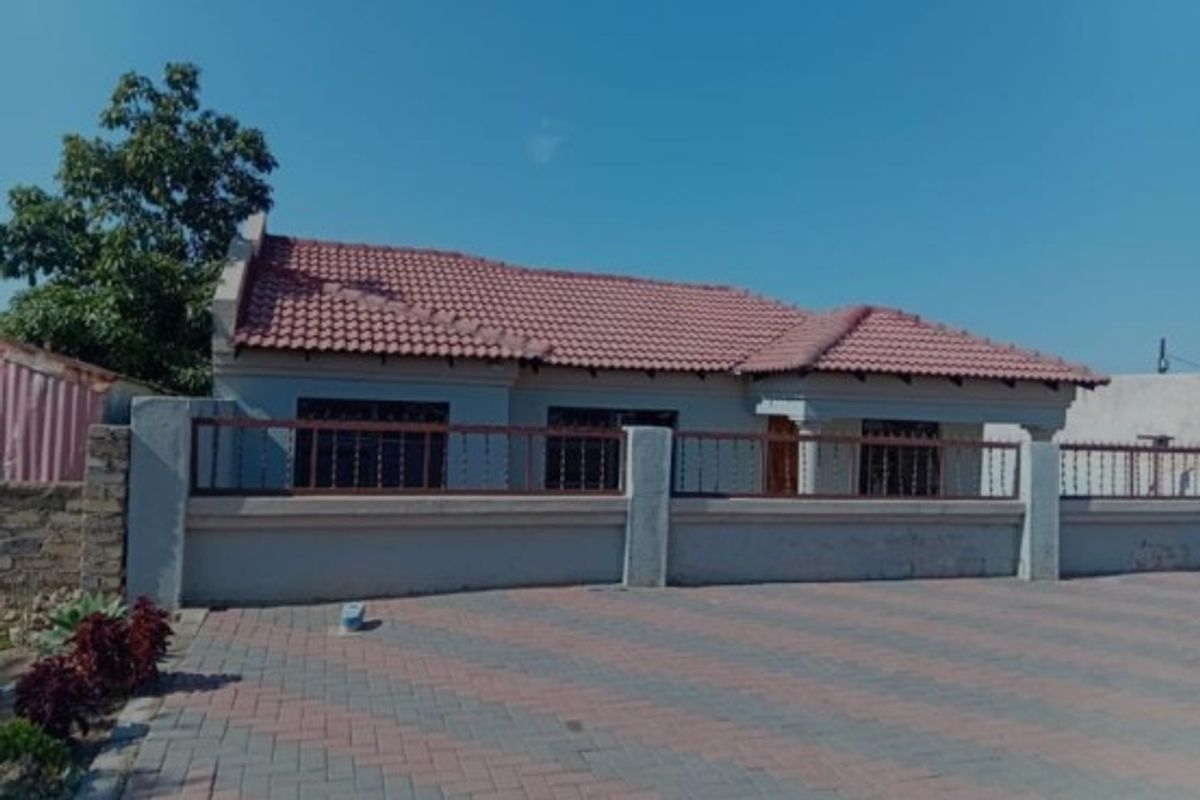 Front exterior view of the property featuring a tiled roof, paved driveway, and a secure boundary wall with metal fencing.