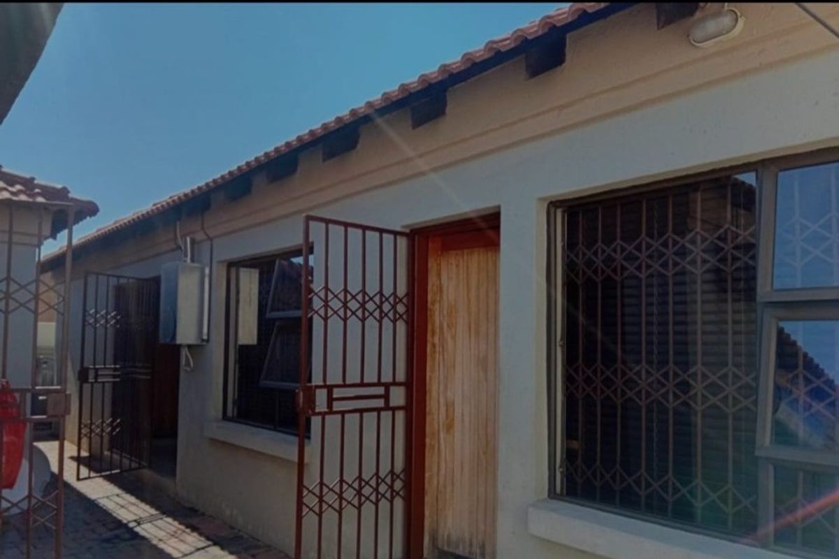 Rear exterior view of the apartment featuring a paved walkway, security gates, and a timber entrance door.