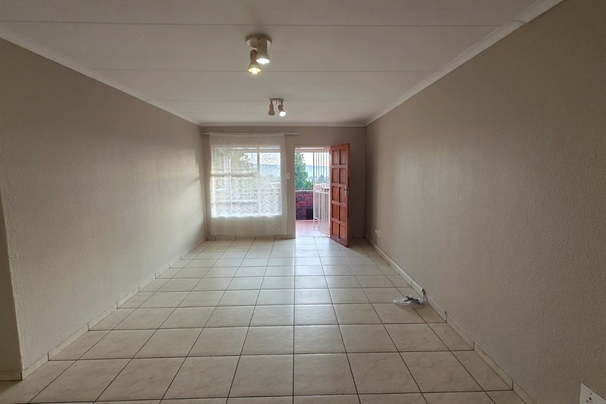 A spacious, empty living room featuring neutral tiled flooring, ceiling lighting, and direct access to an outdoor patio area.