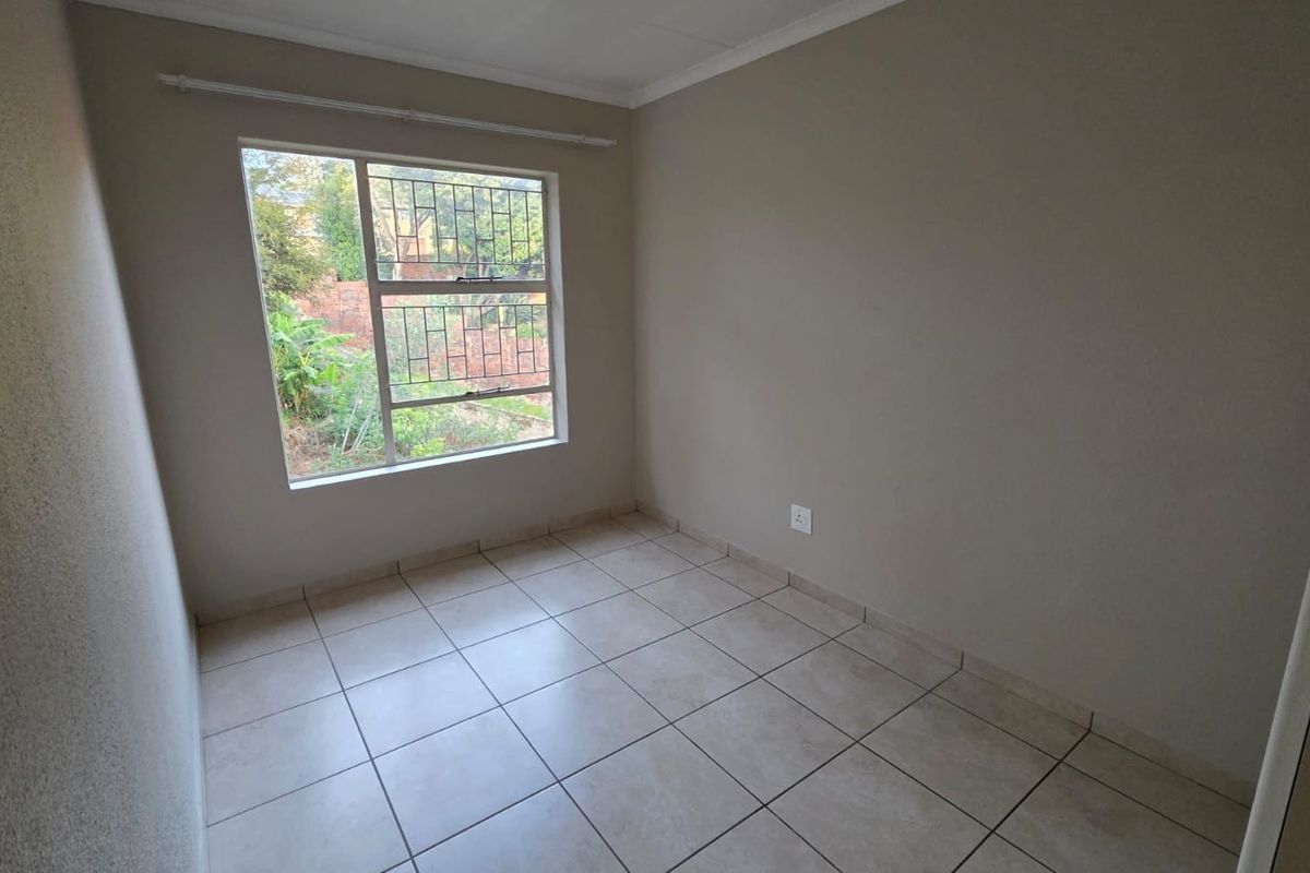 A clean, empty bedroom featuring neutral wall tones, tiled flooring, and a window fitted with security bars.