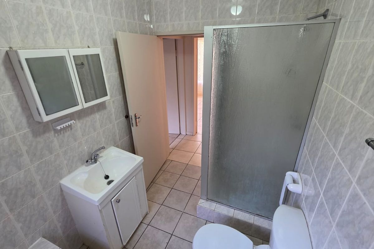 A functional bathroom featuring a shower enclosure, vanity basin, and tiled finishes throughout, presenting a clean and neutral space ready for updates.