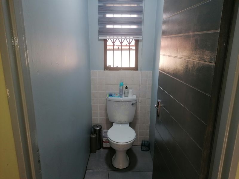 A compact guest bathroom featuring a standard toilet, tiled splashback, and a window with security bars.