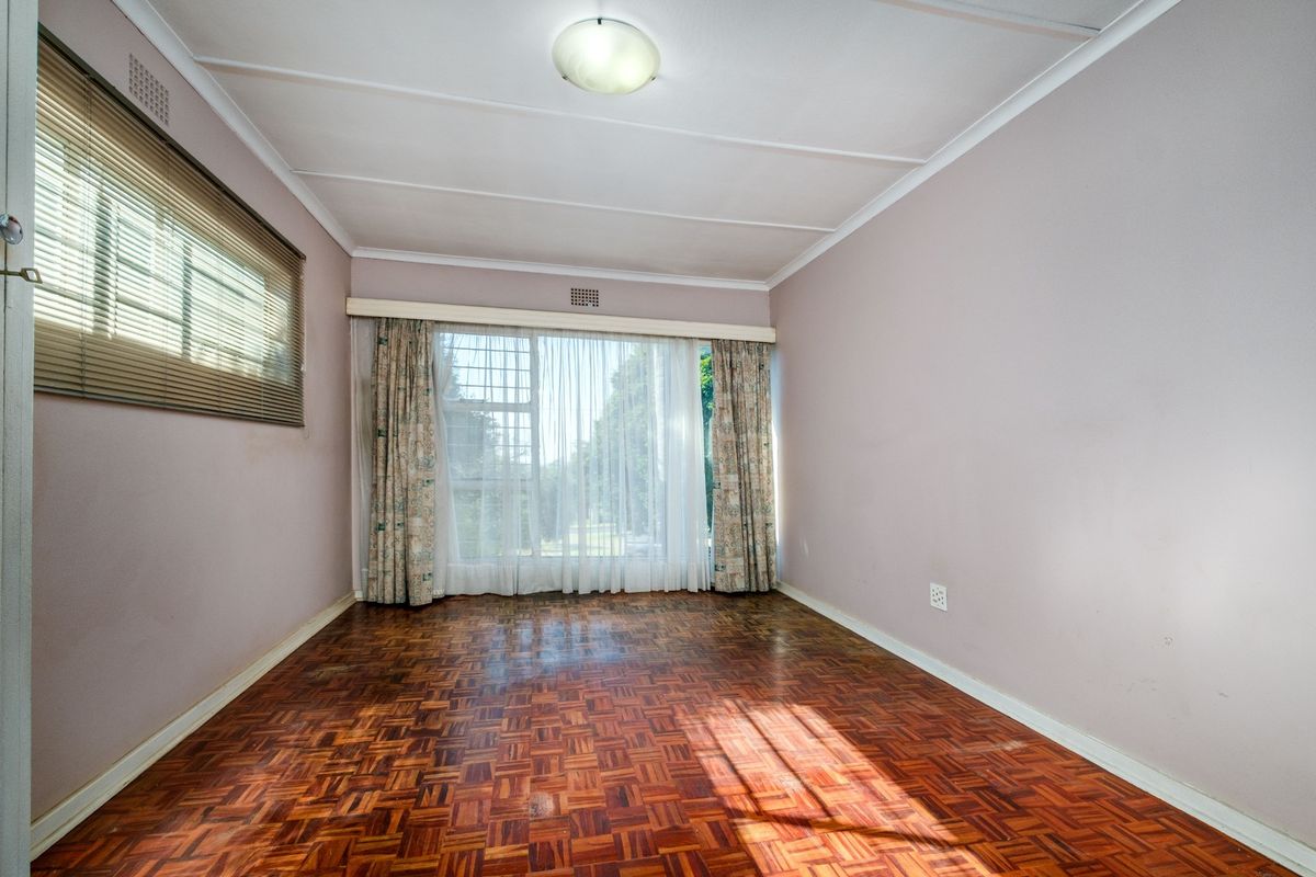 A vacant bedroom featuring original parquet flooring, large windows with curtain tracks, and a neutral wall finish, offering a blank canvas for renovation.