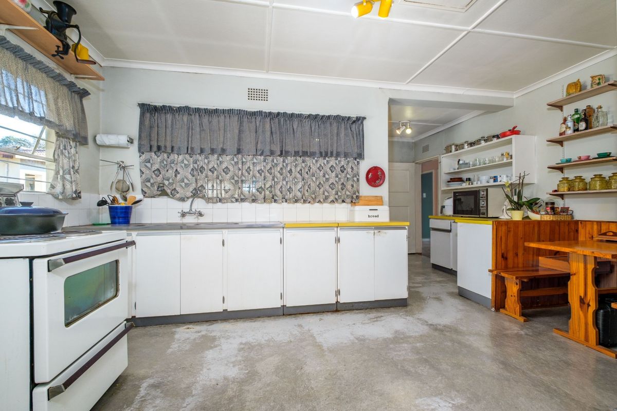 A functional kitchen featuring white cabinetry, a stainless steel sink, tiled backsplash, and a freestanding stove, offering potential for modernization and cosmetic updates.