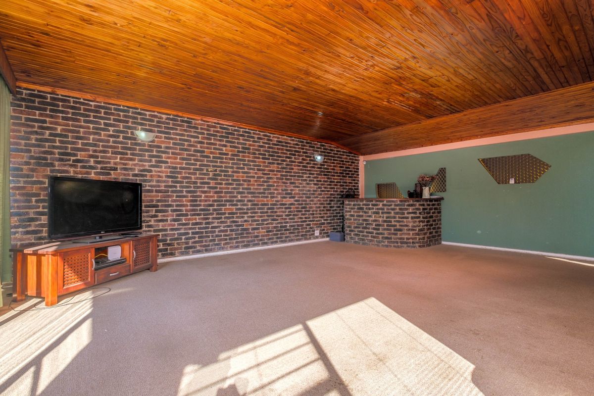 Spacious living room featuring a distinctive exposed brick wall, timber ceiling, and a built-in brick bar area, offering significant potential for modernization.
