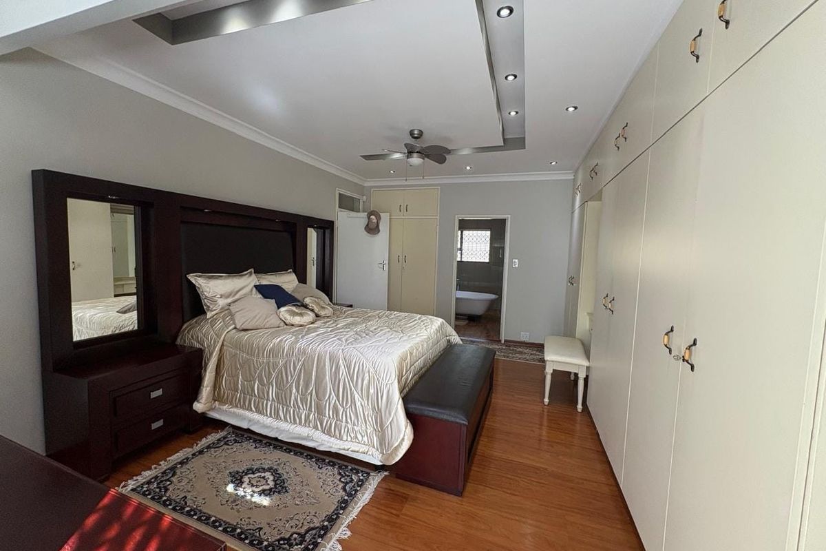 Spacious bedroom featuring extensive built-in cabinetry, hardwood flooring, a modern recessed ceiling design with integrated lighting, and direct access to an en-suite bathroom.