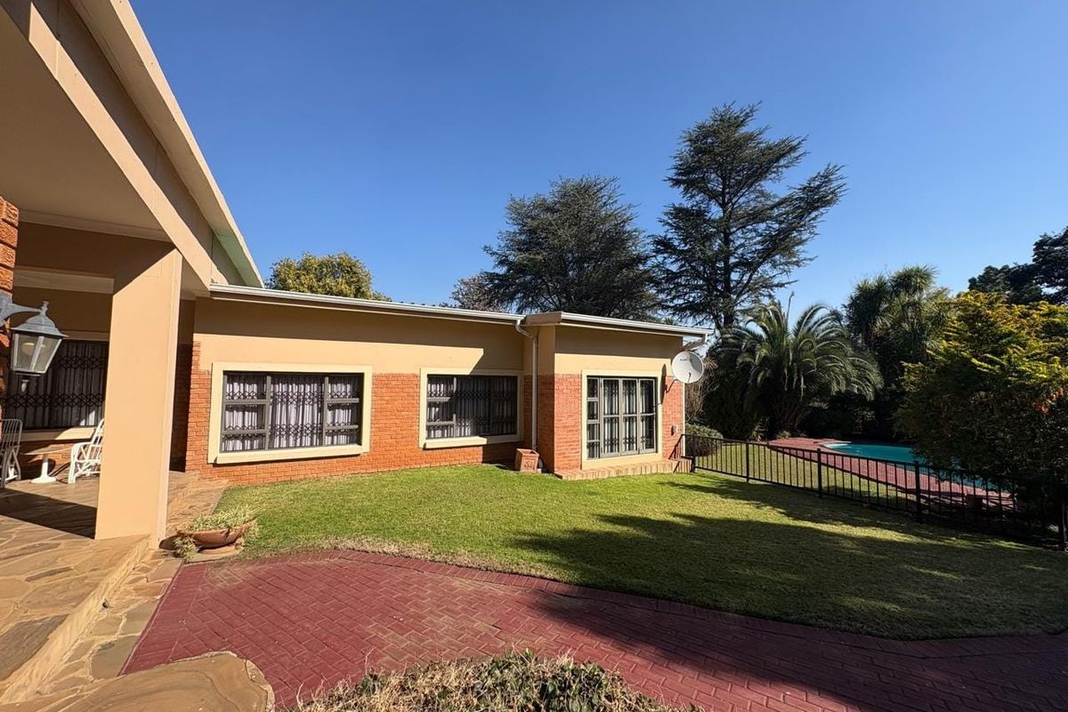 Rear view of the house featuring a brick facade, paved patio area, well-maintained lawn, and a swimming pool in the garden.