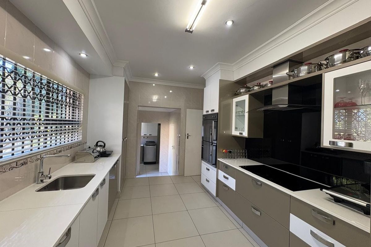 Modern kitchen featuring sleek two-tone cabinetry, stone countertops, integrated appliances, and tiled flooring with direct access to a utility area.