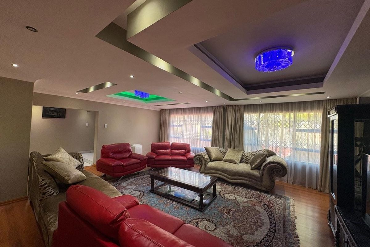 Spacious living room featuring a decorative recessed ceiling with integrated lighting, laminate flooring, and large windows with security bars.