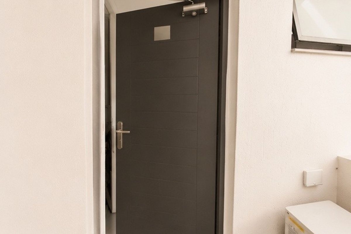 A clean interior entry area featuring a modern dark grey door with a mechanical closer and a small top-hung window.