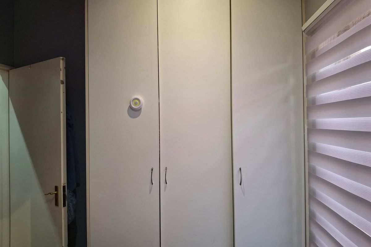 A bedroom featuring white built-in cupboards and modern roller blinds on the window.