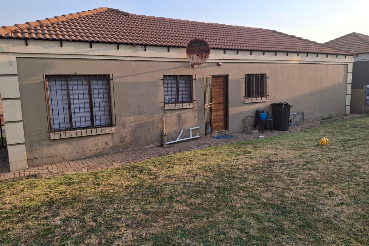 Rear view of the house featuring a tiled roof, security bars on windows, and a paved walkway leading to the back entrance.