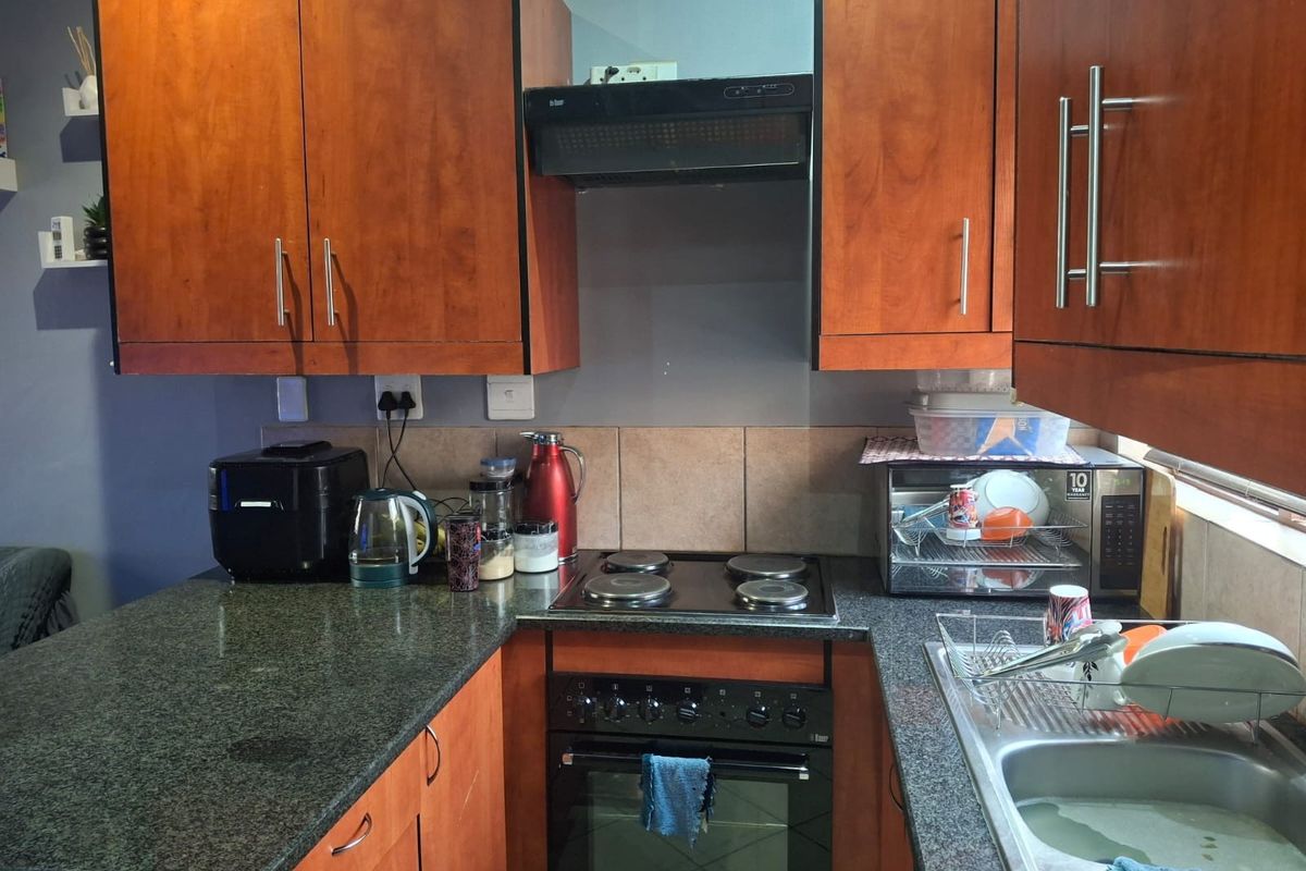Compact kitchen featuring granite countertops, built-in oven, electric hob, extractor fan, and wooden cabinetry with a tiled backsplash.