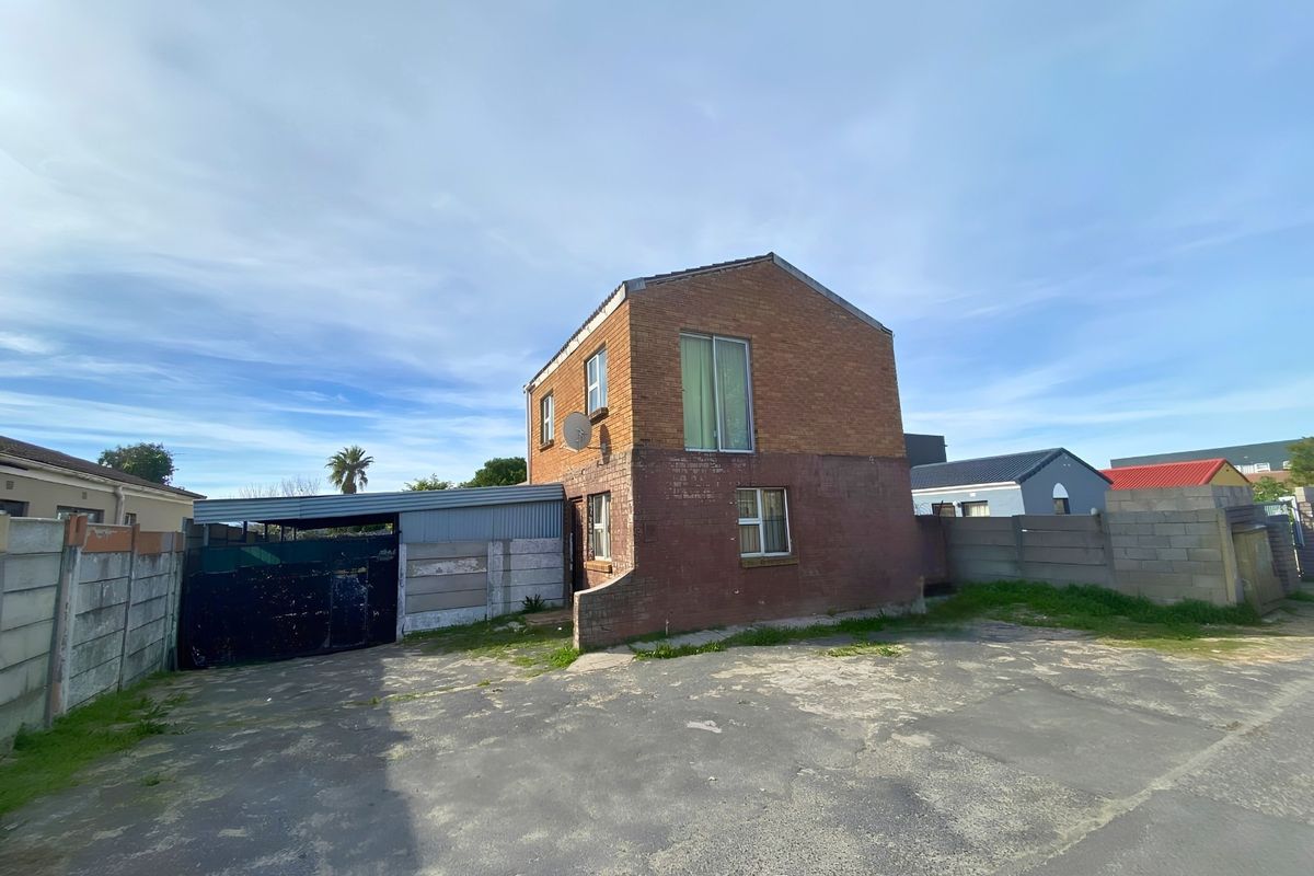 Rear view of a two-story brick house featuring a concrete driveway, metal carport, and enclosed yard with precast concrete boundary walls.