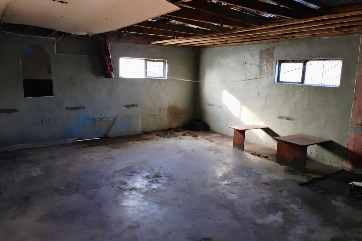 An unfinished, vacant interior space featuring exposed timber ceiling rafters, concrete flooring, and plastered masonry walls, requiring significant renovation and finishing work.
