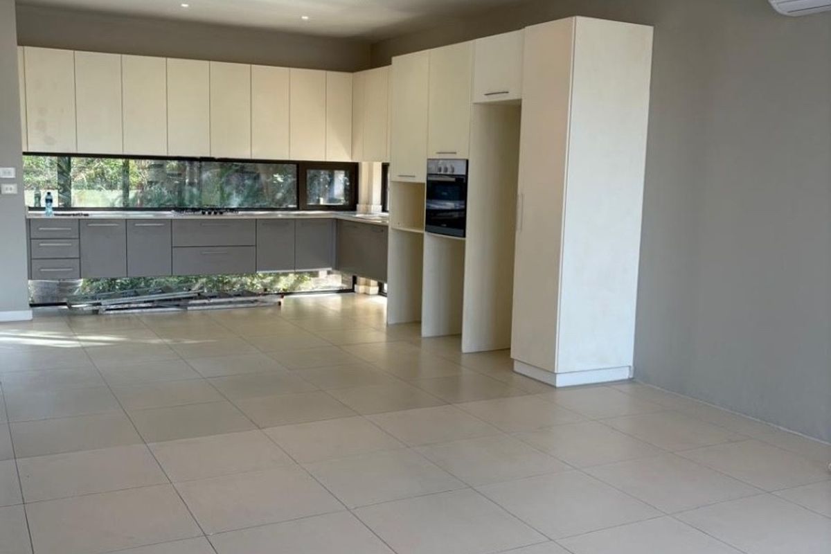 Modern open-plan kitchen featuring two-tone cabinetry, built-in oven, tiled flooring, and recessed lighting in a spacious, neutral-toned interior.