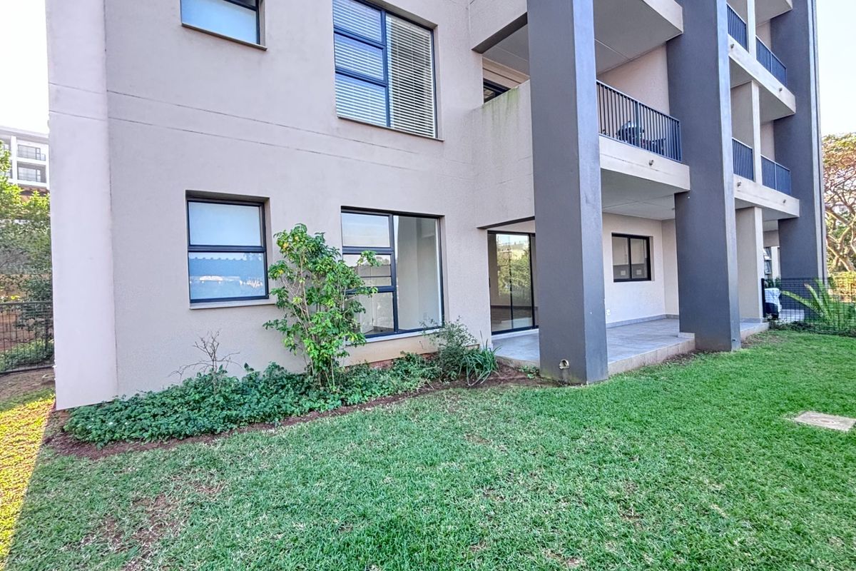 Rear view of a modern apartment building featuring a ground floor patio, lawn area, and multi-level balconies with metal railings.