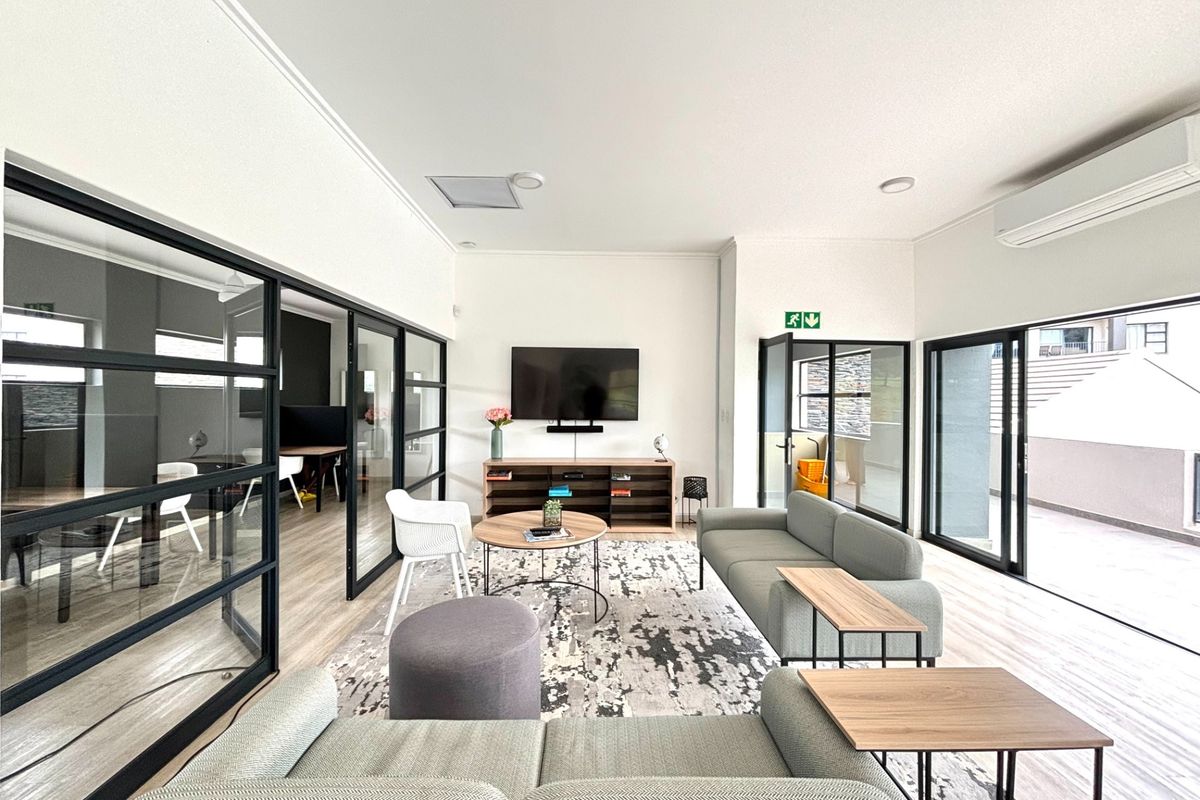 Modern living room featuring sleek black-framed glass partitions, wood-look flooring, and large sliding doors leading to an outdoor area.