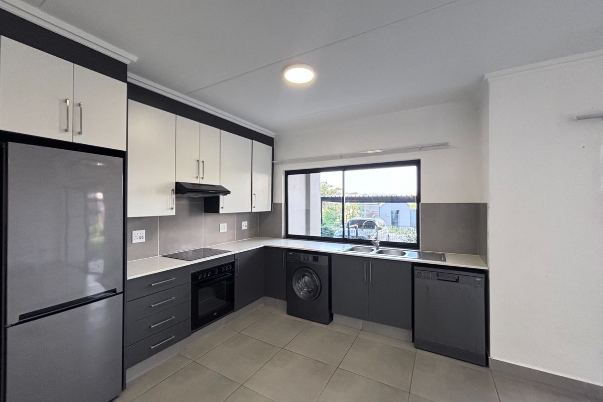 Modern kitchen featuring two-tone cabinetry, stone countertops, integrated oven and hob, and tiled flooring with ample space for appliances.